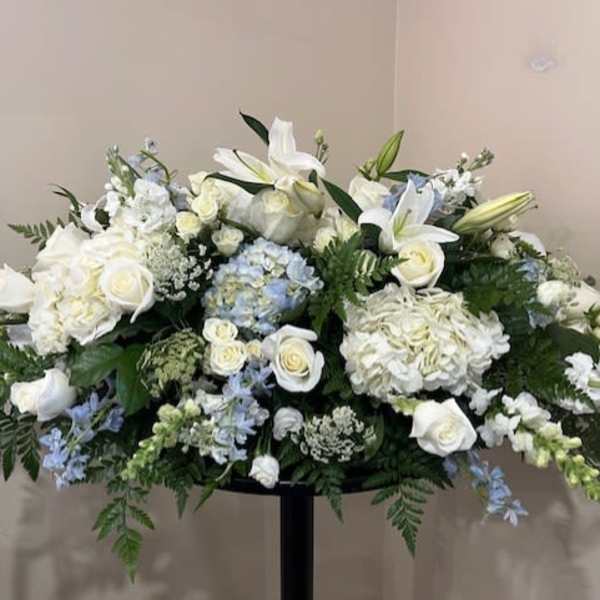 Large white floral arrangement with lilies, roses, and hydrangeas on a stand