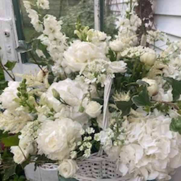White floral arrangement with roses, hydrangeas, and snapdragons in a basket