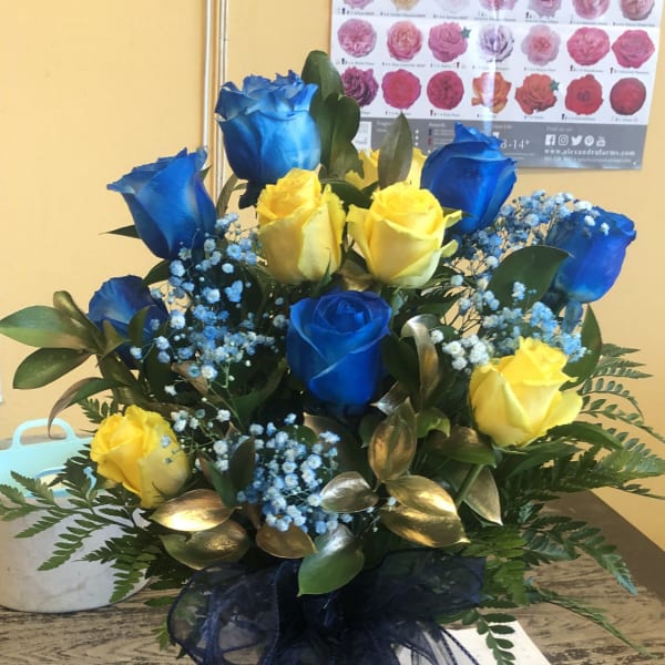 Blue and yellow roses arranged in a glass vase with a dark ribbon