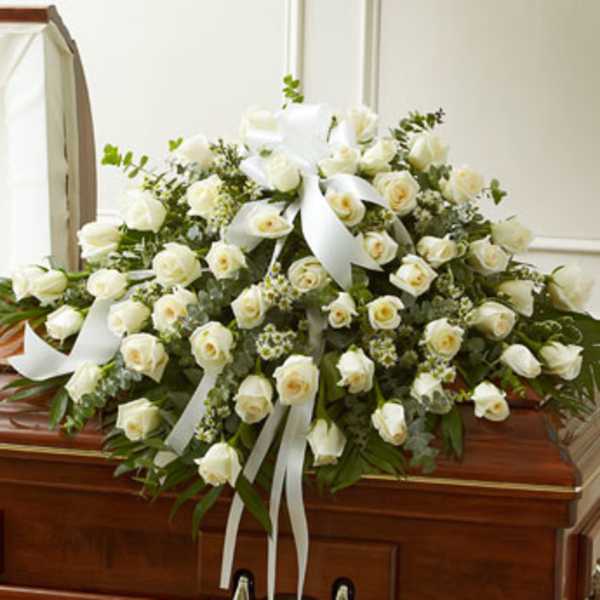 White rose casket spray with ribbon on a wooden casket