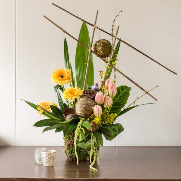 Tall floral arrangement with yellow blooms, pink tulips, and decorative branches
