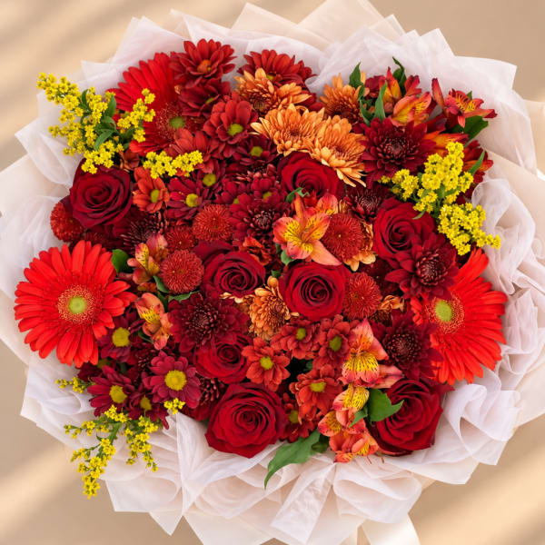 Bouquet of red roses, orange daisies, and yellow filler flowers wrapped in white paper
