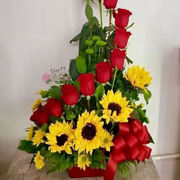 Tall arrangement of red roses and yellow sunflowers with a red bow