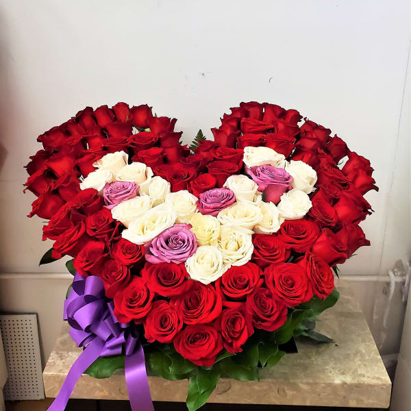 Heart-shaped bouquet of red, white, and purple roses with a purple ribbon