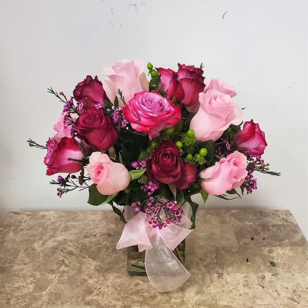 Pink and burgundy roses in a glass vase with a pink ribbon