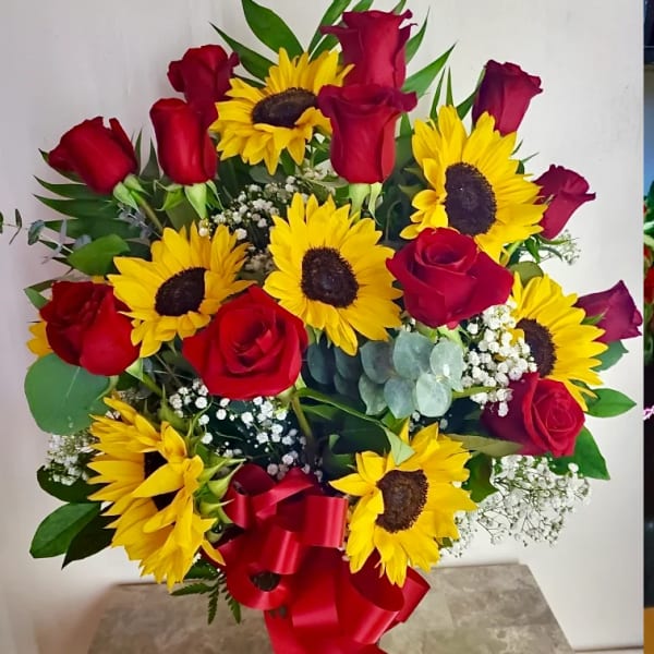 Bouquet of red roses and yellow sunflowers in a vase with a red ribbon