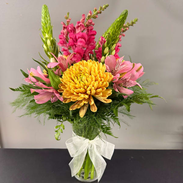 Pink and yellow mixed bouquet in a clear glass vase with a white bow