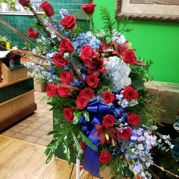 Large standing floral spray with red roses, blue hydrangeas, and lilies