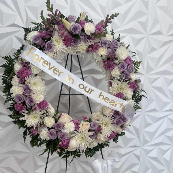 Floral memorial wreath on an easel with a ribbon reading "Forever in our hearts"
