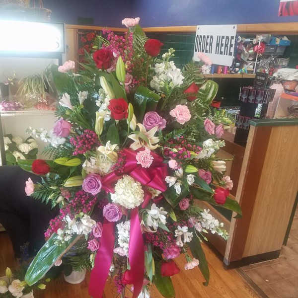Large standing floral spray with roses, lilies, and pink ribbon