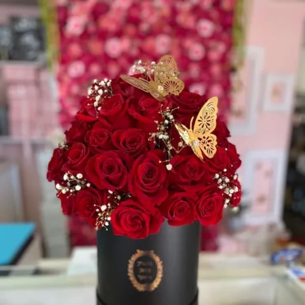 Red roses arranged in a black hatbox with gold butterfly accents