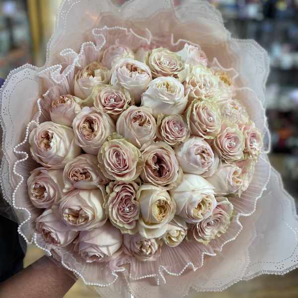 Bouquet of pale pink and cream roses wrapped in lace-like paper