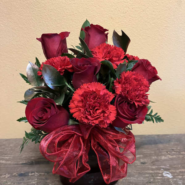 Red rose and carnation arrangement in a black vase with a red ribbon