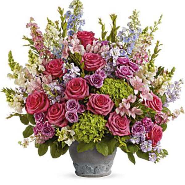 Abundant pink and purple mixed flower arrangement with green hydrangeas in a gray ceramic pot