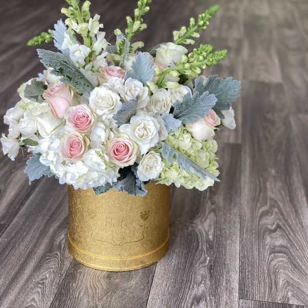 Pink and white roses arranged in a gold round box