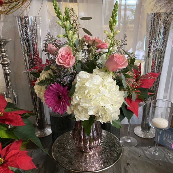 Pink roses and white hydrangeas in a metallic vase with red poinsettias nearby.