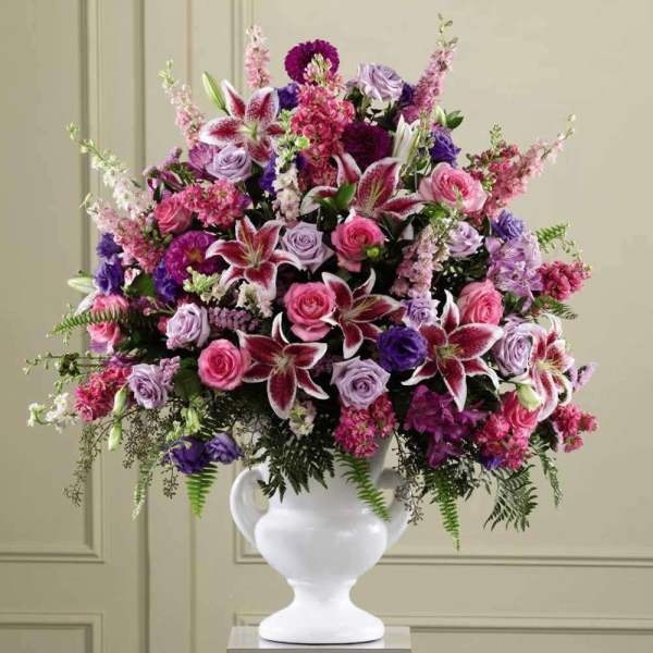 Large pink and purple flower arrangement with lilies and roses in a white urn vase