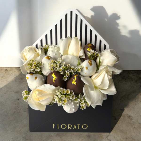 White roses and chocolate-covered strawberries in a striped gift box