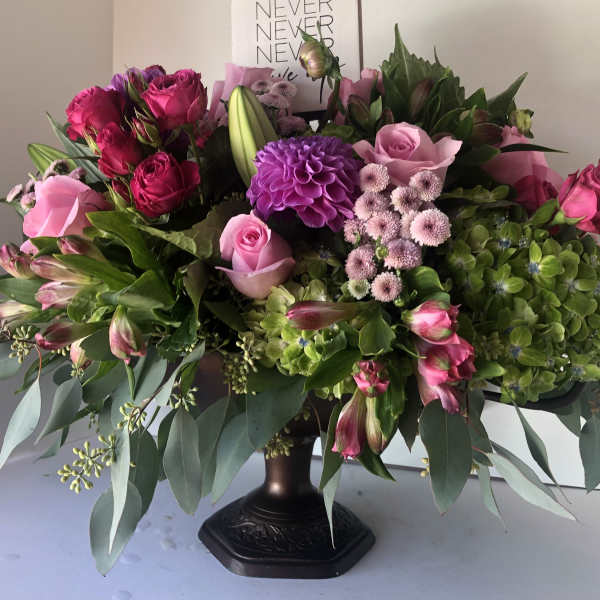 Large pink and purple floral arrangement in a dark pedestal vase
