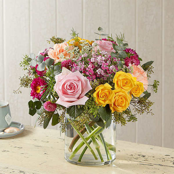 Mixed bouquet of pink, yellow, and peach flowers in a clear glass vase
