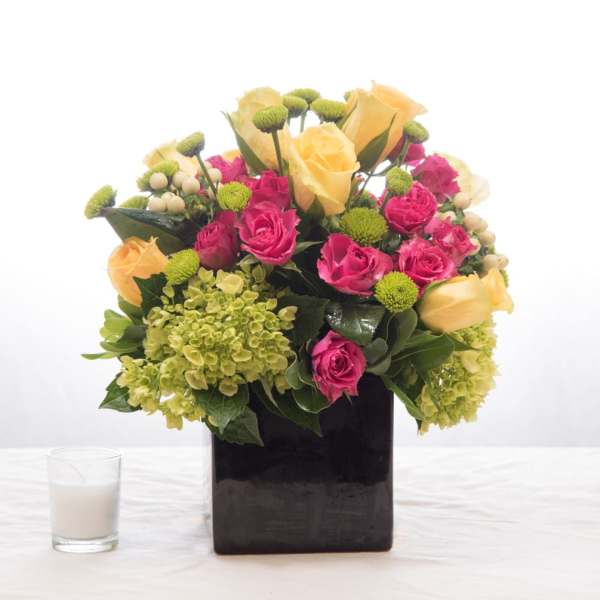Pink and yellow roses in a black square vase with green accents