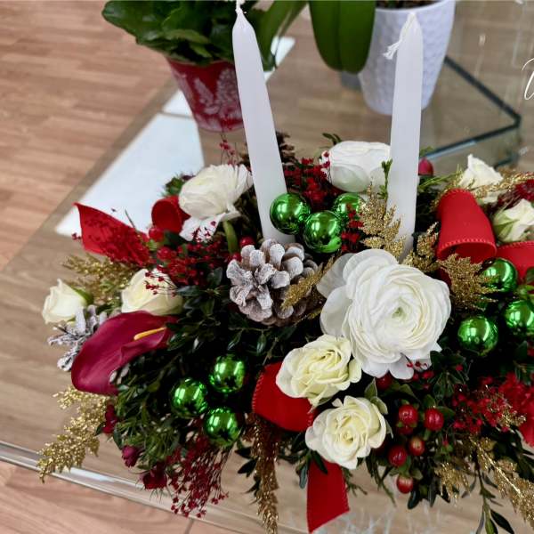 Holiday centerpiece with white flowers, red accents, and two white taper candles