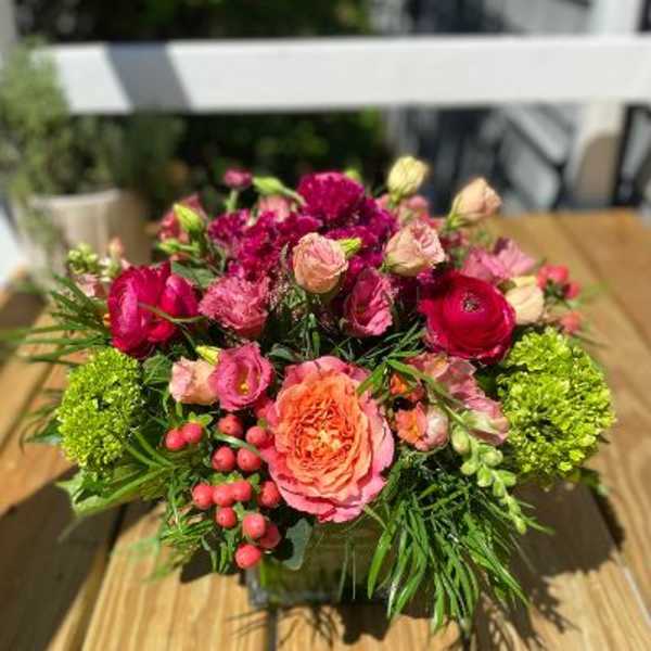 Pink and red mixed flower arrangement in a square container