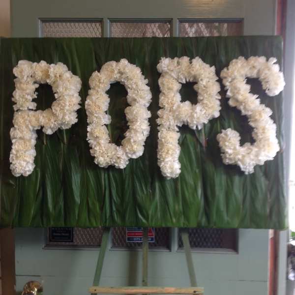 White floral letters spelling "POPS" on a green backdrop.