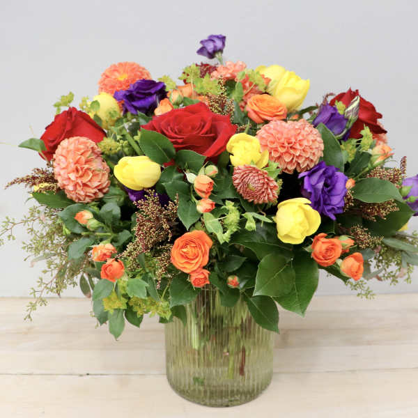 Mixed bouquet of roses, tulips, and dahlias in a glass vase