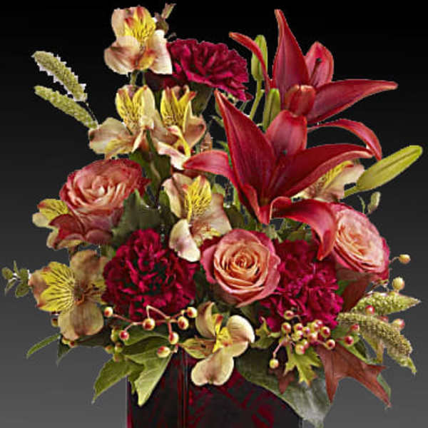 Mixed bouquet with red lilies, pink roses, and burgundy flowers in a glass vase