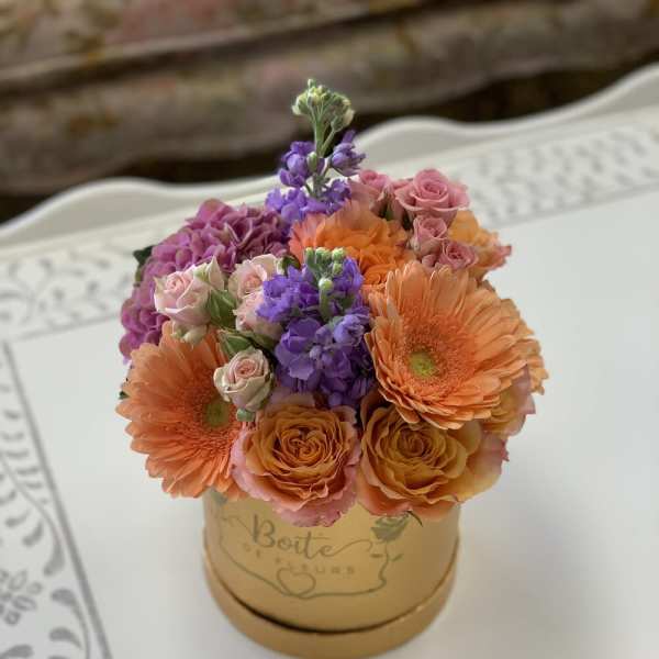 Bouquet of orange gerberas, pink roses, and purple flowers in a gold box