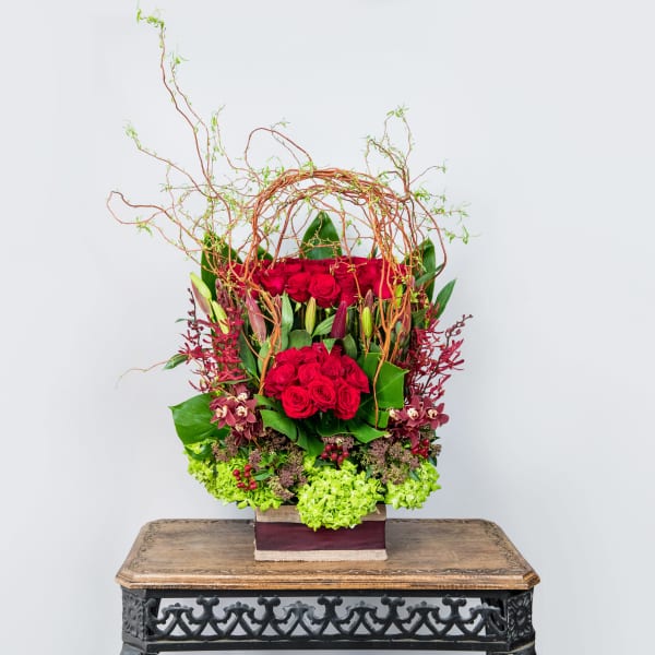 Tall arrangement of red roses with green accents in a square container