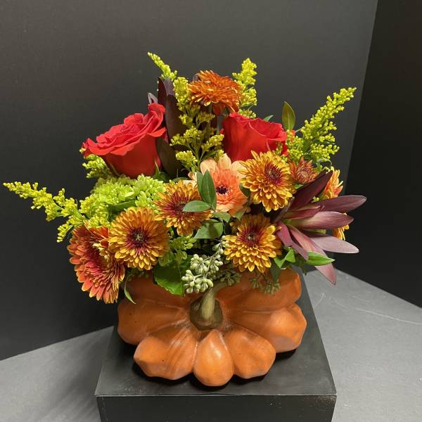 Autumn floral arrangement in a pumpkin-shaped container with red roses and orange blooms