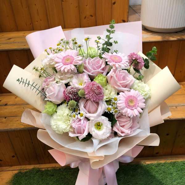 Bouquet of pink roses, gerbera daisies, and mixed blooms wrapped in pastel paper