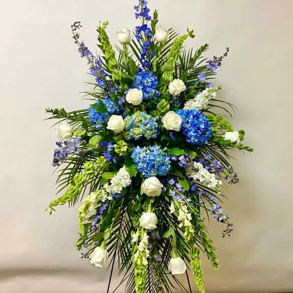 Tall standing floral spray with blue hydrangeas, white roses, and purple flowers