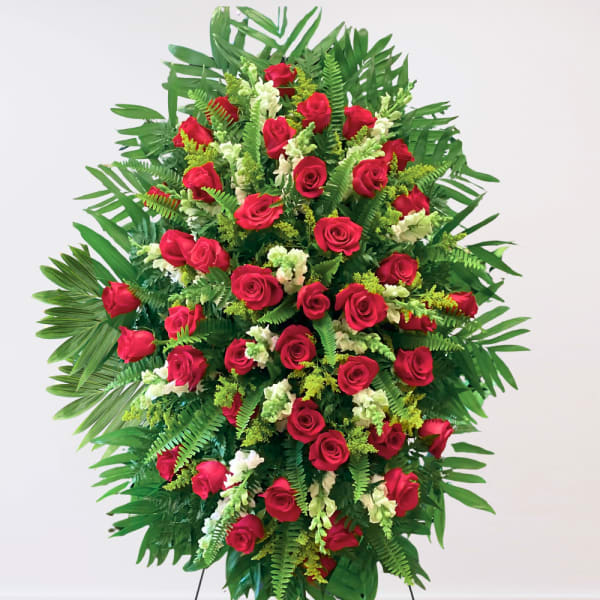 Standing spray of red roses with white accents and tropical greenery