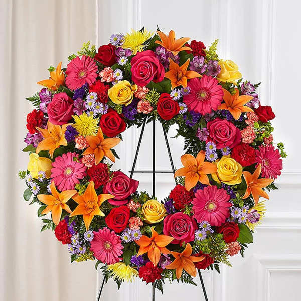 Colorful floral wreath on a black stand with roses, lilies, and daisies