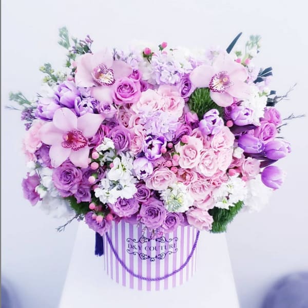 Large pink and purple flower arrangement in a striped hat box