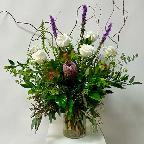White roses and purple spikes in a glass vase with mixed greenery