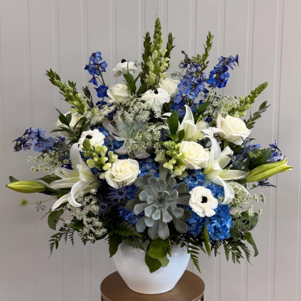 Blue and white floral arrangement in a white vase with lilies and roses