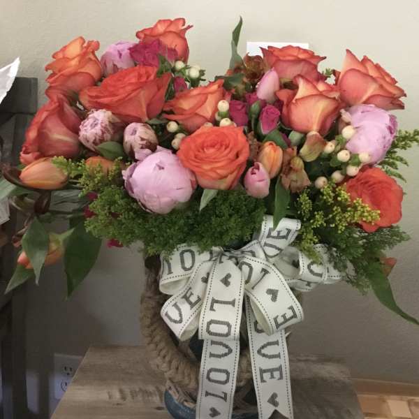 Bouquet of orange roses and pink peonies in a woven vase with a LOVE ribbon