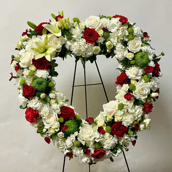 Heart-shaped floral wreath with red, white, and green flowers on a stand