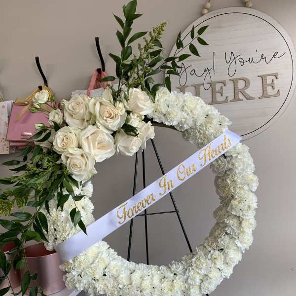 White rose and carnation heart wreath on an easel with a ribbon