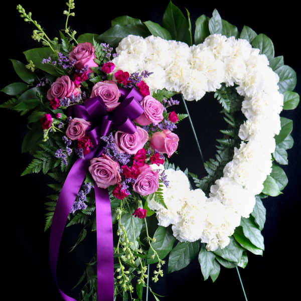 Heart-shaped floral wreath with white carnations and pink roses on a black stand