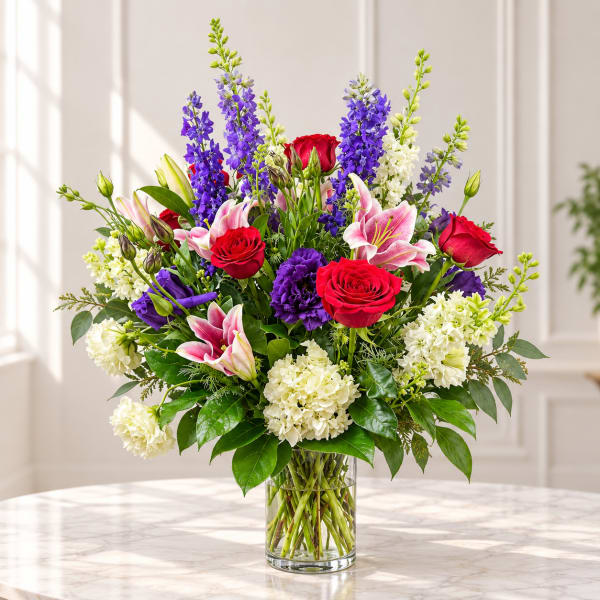 Mixed bouquet of red roses, pink lilies, purple blooms, and white flowers in a glass vase
