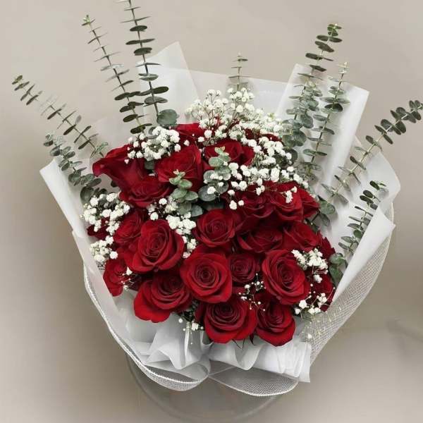 Hand-tied bouquet of red roses with white filler flowers and tall greenery wrapped in white paper.