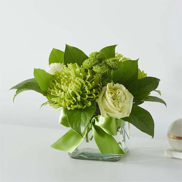 Green and white floral arrangement in a clear glass vase with a ribbon