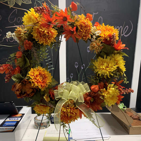 Autumn wreath with orange and yellow flowers and a pale ribbon bow