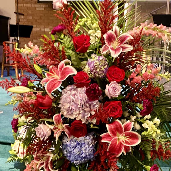 Large standing floral arrangement with roses, lilies, and hydrangeas