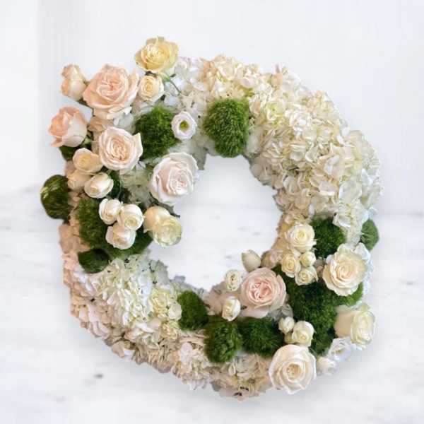 Circular floral wreath with white hydrangeas, cream roses, and green moss accents